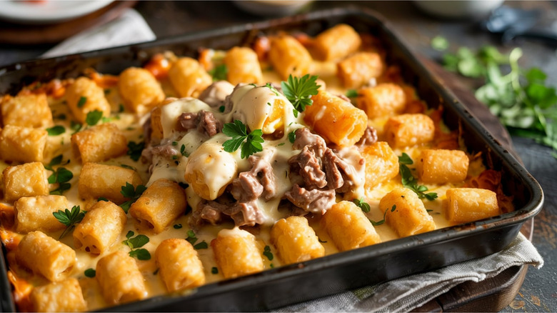 Cazuela de tater tot con queso en un plato sobre una mesa con perejil adicional al fondo.