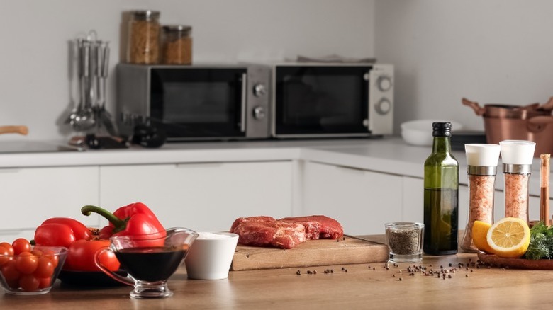 Un filete de ternera en una encimera de cocina de madera rodeado de pimiento rojo y condimentos en una cocina