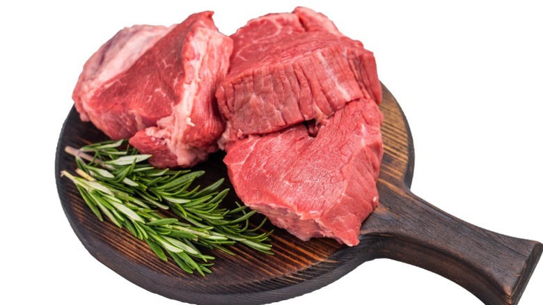 Tres trozos de filet mignon crudo sobre una tabla de servir de madera con ramitas de romero