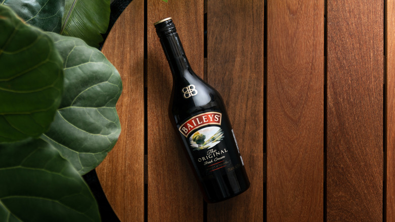 Una botella de crema irlandesa de Bailey's sobre una mesa marrón con hojas verdes