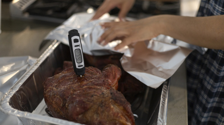 Termómetro para carne en costillas mientras se encuentra en una bandeja cubierta con papel de aluminio con dos manos