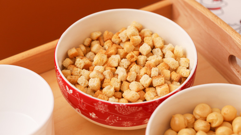 Crutones sentados en un nowl rojo y blanco junto a un plato de garbanzos
