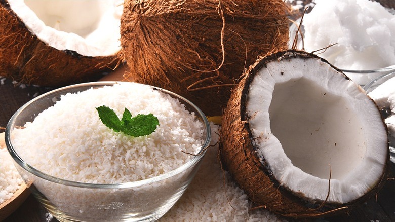 Un plato de hojuelas de coco rodeado de cocos enteros.