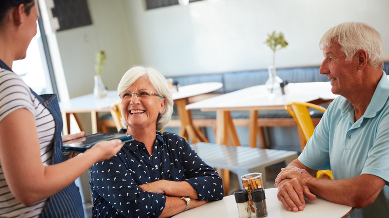Un camarero esperando a una pareja de ancianos en una cafetería.