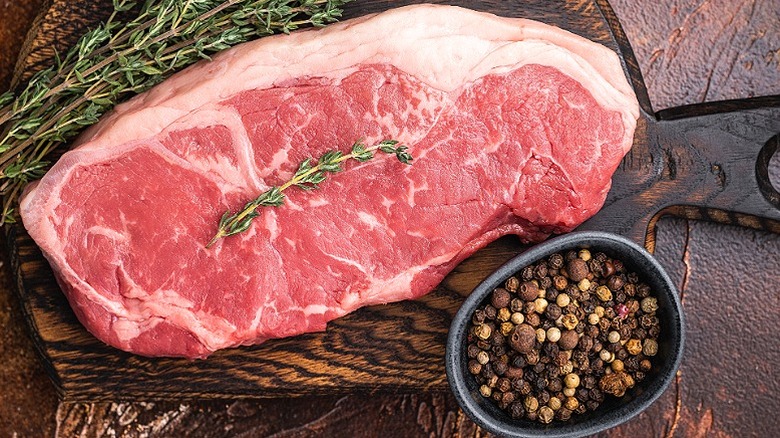 Filete de ternera cruda de Nueva York sobre una tabla de madera.