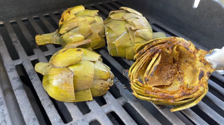 4 mitades de alcachofa asadas boca abajo, con una cara carbonizada sostenida con unas pinzas