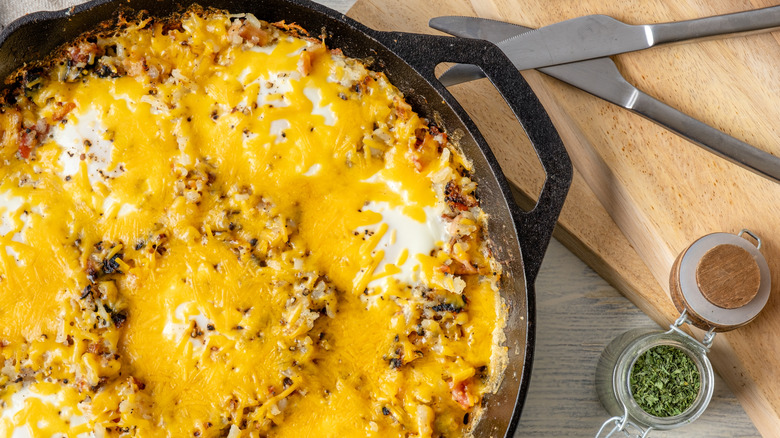 Patatas fritas cubiertas con queso en una sartén con pequeños frascos de hierbas al lado