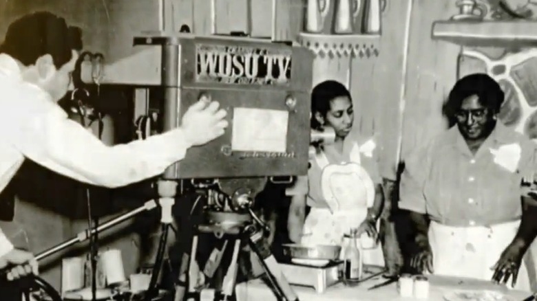 Lena Richard en 1949 o 50, cocinando frente a una cámara de televisión WDSU con otra mujer negra parada a su derecha.