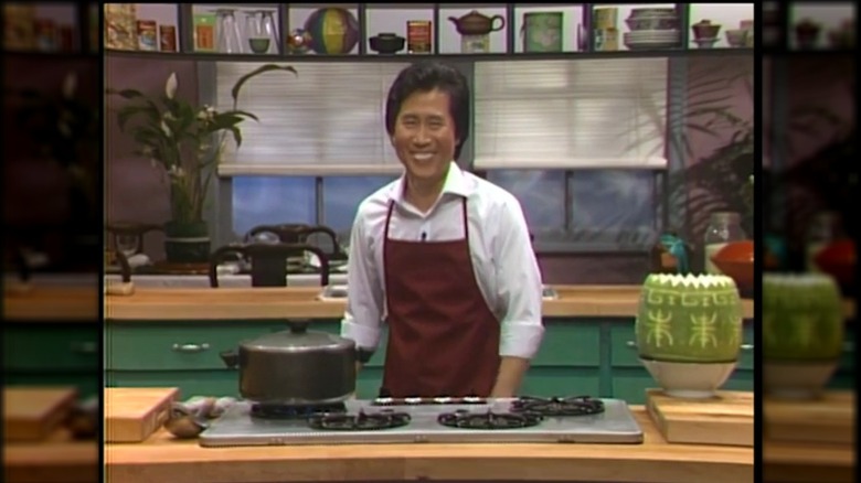 El chef Martin Yan en la década de 1980, sonriendo con un delantal rojo y una camisa blanca, en el set de 