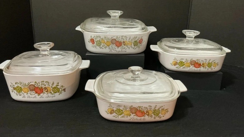 Un juego CorningWare de 8 piezas con 4 tapas transparentes y 4 cacerolas con coloridos diseños vegetales.
