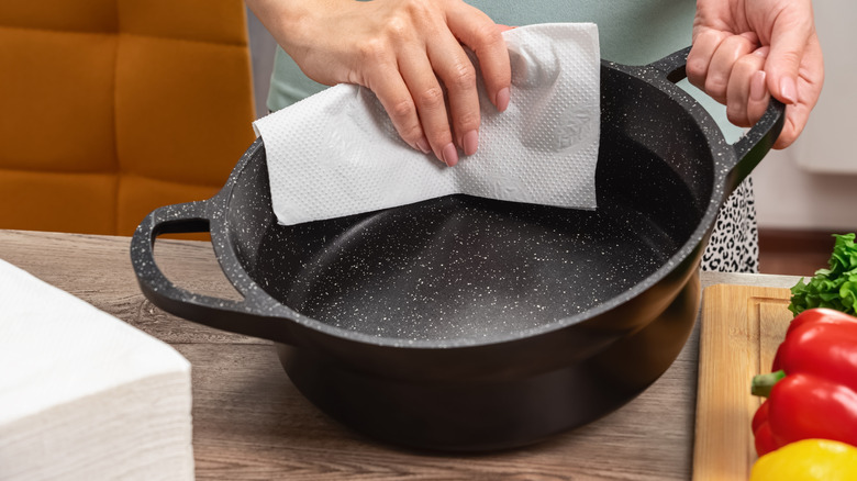 Una persona limpia una olla de hierro fundido con una toalla de papel para asegurar un secado adecuado.