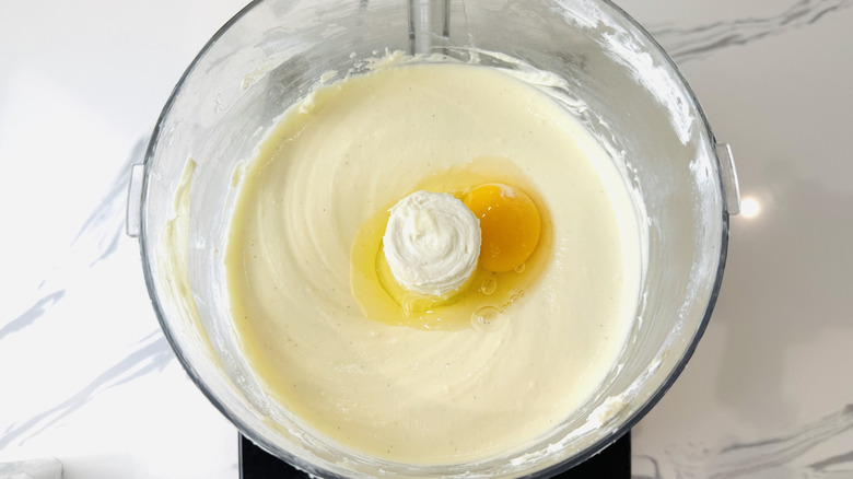 Agregar huevos a la masa de tarta de queso en un procesador de alimentos