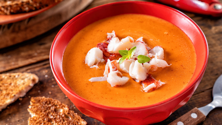 Tazón de sopa de langosta en un recipiente rojo junto a una tostada