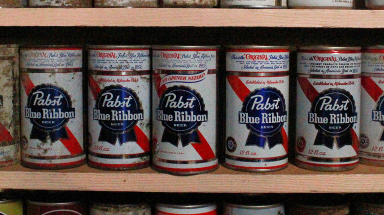 Una fila de latas antiguas de Pabst Blue Ribbon, algunas comenzando a oxidarse, en exhibición
