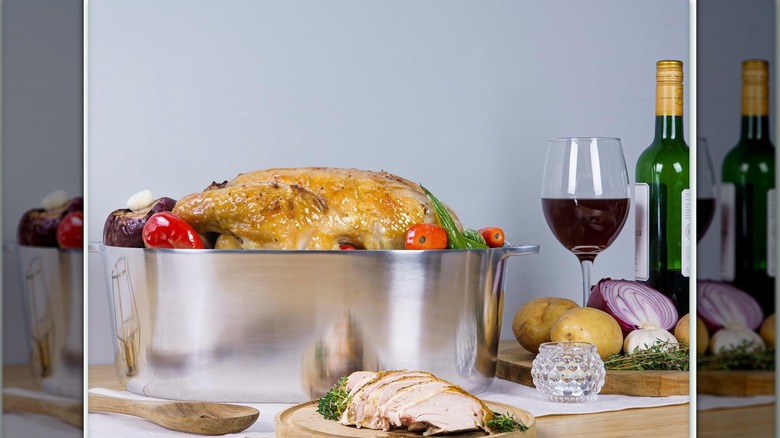 Una olla de aluminio MAGNAWARE con un pavo asado en el interior con pavo en rodajas, vino tinto y verduras sobre la mesa.