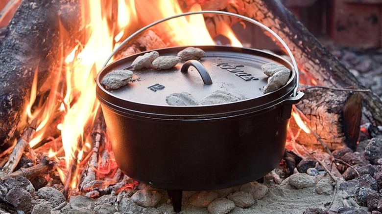 Un horno holandés Lodge Camp en negro, sentado dentro de una fogata con brasas en la tapa