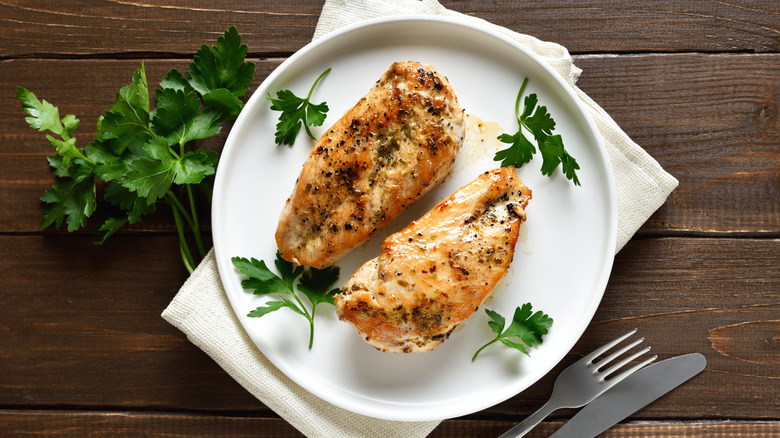Pechugas de pollo asadas, deshuesadas y sin piel, con condimentos y perejil en un plato blanco