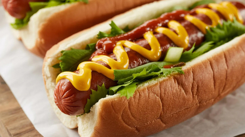 Un hot dog en panecillo con verduras de hojas verdes, un poco de ketchup y mostaza amarilla prominente.