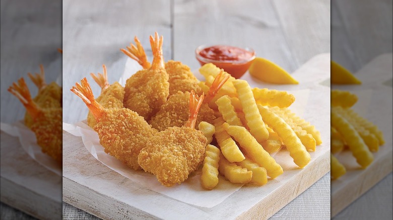 Camarones Butterfly Jumbo de Culver sobre una tabla de cortar con papas fritas y salsa para mojar.