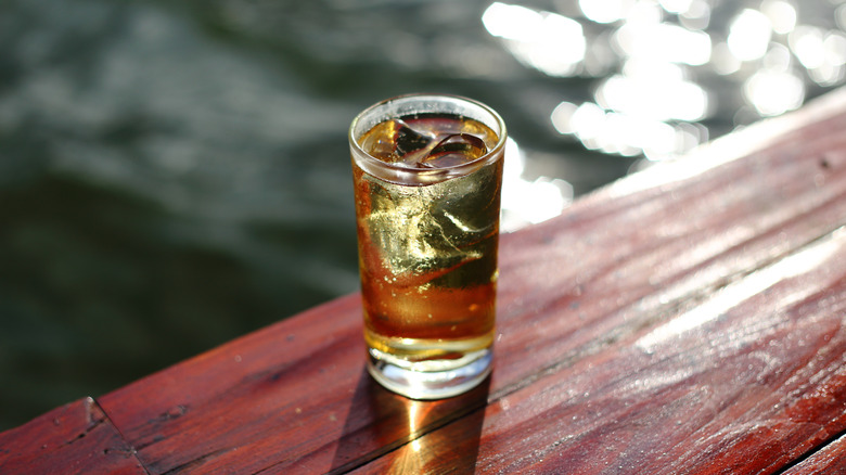 Bebida marrón sobre hielo en un vaso alto junto al agua