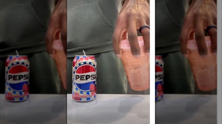 La mano de una mujer agitando una taza con una Pepsi sucia junto a una lata de Pepsi de cereza