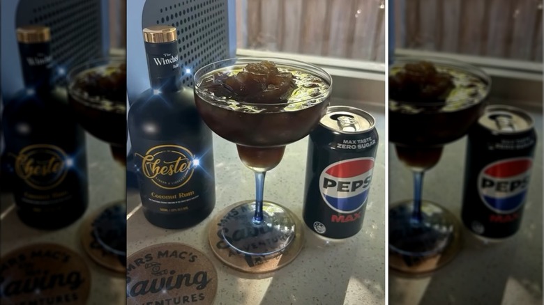 Vaso de margarita con bebida marrón helada junto a ron de coco y lata de Pepsi