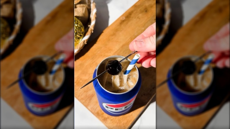 Vista superior de la lata de pepsi llena de bebida helada con pajita y cereza en brocheta