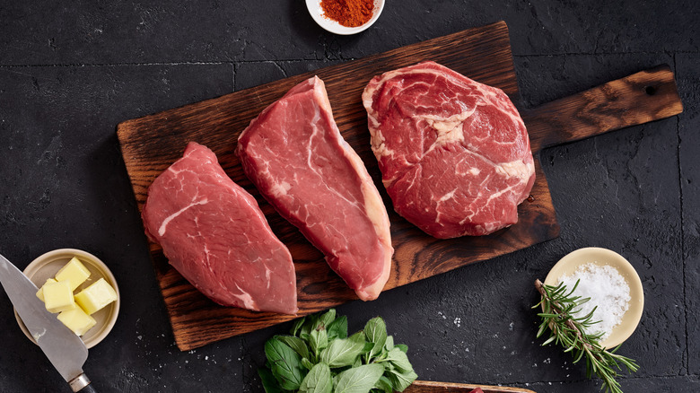Diferentes cortes de carne reposando sobre una tabla de cortar con mantequilla, sal y hierbas