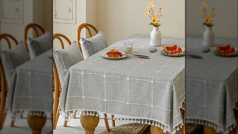 Un mantel gris sobre una mesa de cocina con platos de frutas cortadas y flores encima