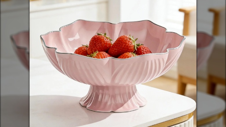 Un cuenco rosa sobre una mesa blanca con fresas