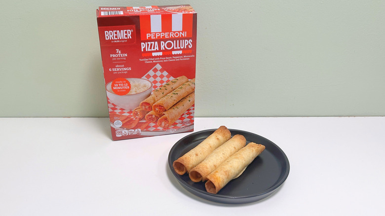 Una caja de rollitos de pizza Bremer Pepperoni junto a rollitos de pizza en un plato negro