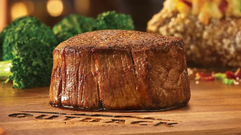 Un filet mignon cocido de 6 onzas sobre una tabla de cortar de madera con el logotipo de Outback Steakhouse
