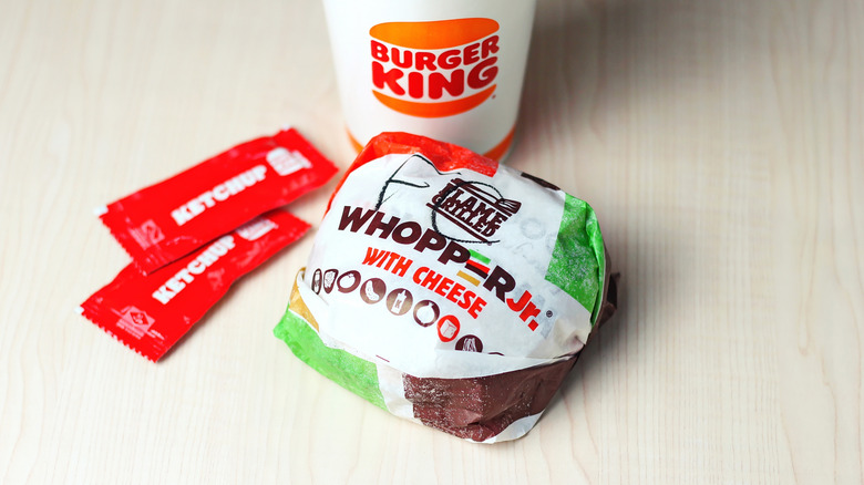 Un Whopper Jr envuelto con queso en Burger King, con sobres de ketchup y bebida