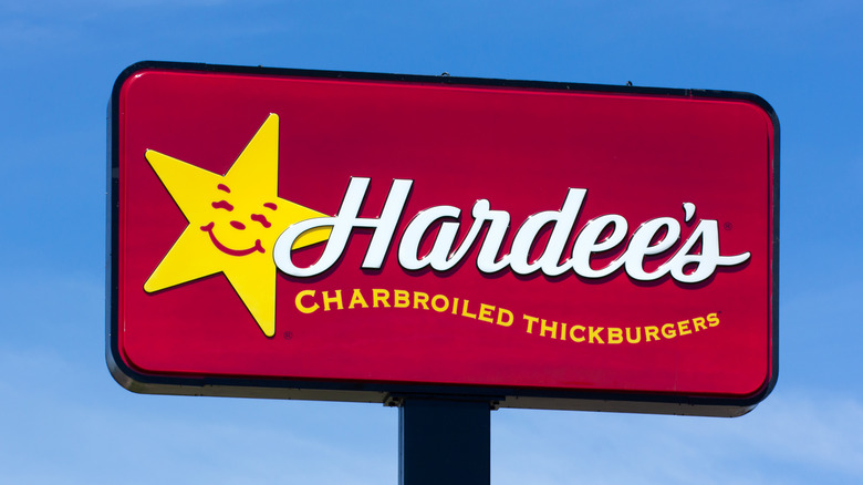 Señalización exterior en Hardee's con el logotipo de una estrella sonriente y un eslogan sobre "hamburguesas gruesas a la brasa"
