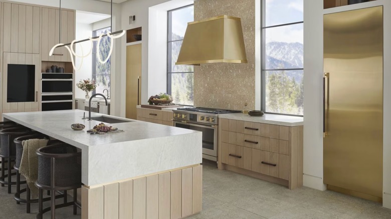 Una cocina moderna con refrigeradores y campana extractora Monogram de latón pulido y una estufa/horno Monogram de acero inoxidable con detalles en latón.