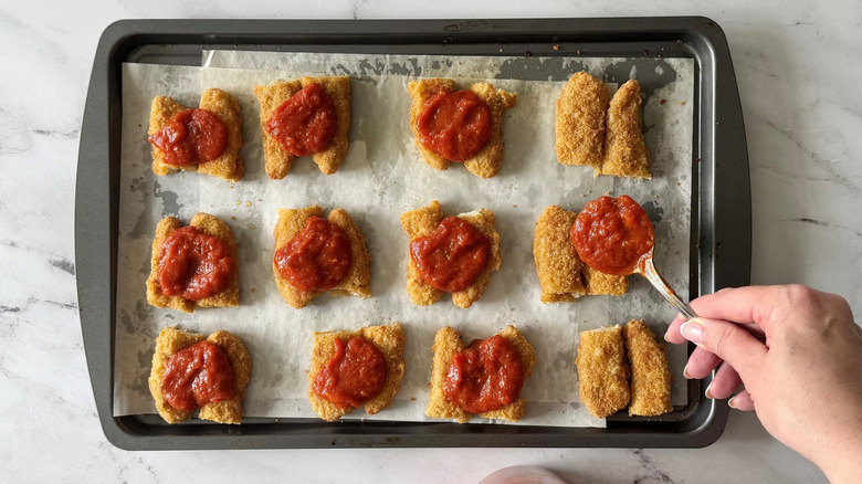 Vierta salsa marinara sobre tiras de pollo en una bandeja para hornear
