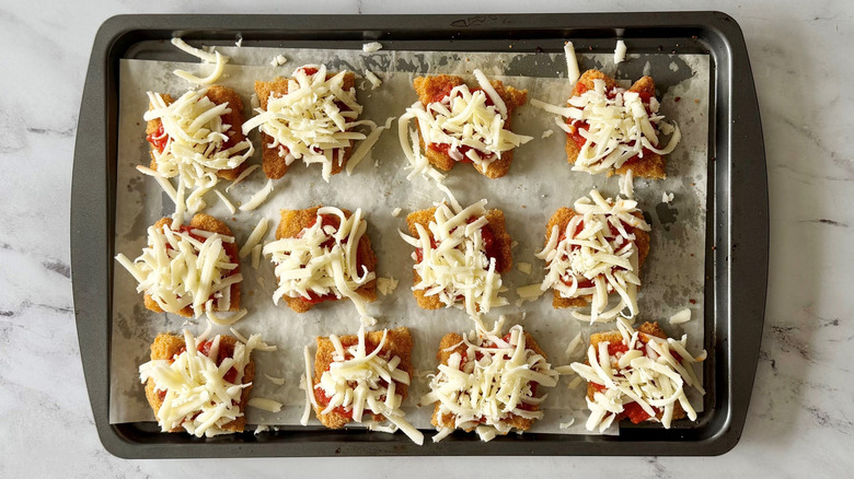 Porciones de tiras de pollo cubiertas con marinara y mozzarella en una bandeja para hornear