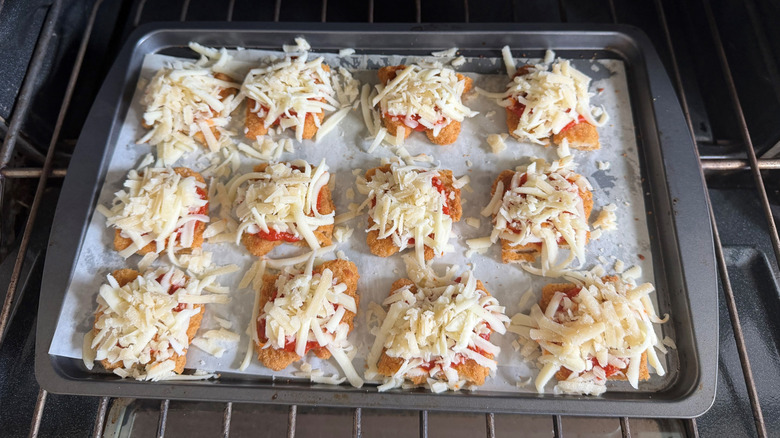 Tiras de pollo cubiertas con marinara y mozzarella en una bandeja para hornear