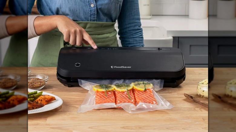Persona que utiliza el aparato sellador al vacío FoodSaver Preserve con bolsas y recipiente para marinar para conservar el salmón