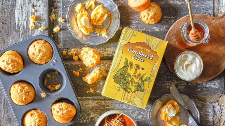 Caja de mezcla de pan de maíz Trader Joe's rodeada de muffins hechos dentro y fuera de latas