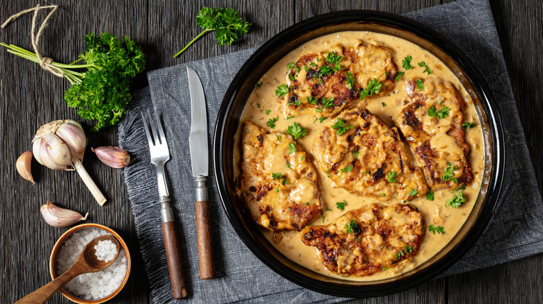 Las chuletas de cerdo deshuesadas y asadas están en una salsa de color marrón claro con perejil picado.