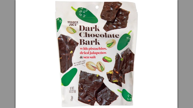 Una bolsa de corteza de chocolate oscuro con pistachos, jalapeños secos y sal marina sobre un fondo blanco.