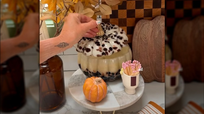 Mano levantando la tapa de la vela con forma de calabaza sobre un pedestal