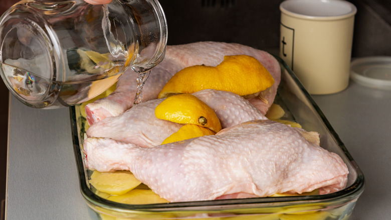 Persona agregando líquido a una fuente de vidrio para hornear con pollo