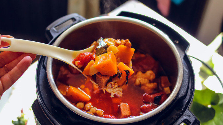 Un guiso de pollo, batatas y tomates dentro de una olla instantánea con un poco de cuchara