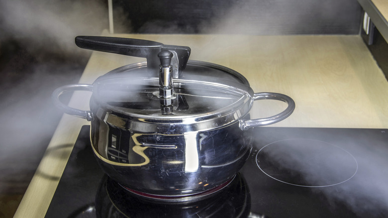 Una olla a presión plateada que expulsa vapor en forma de X en una cocina eléctrica