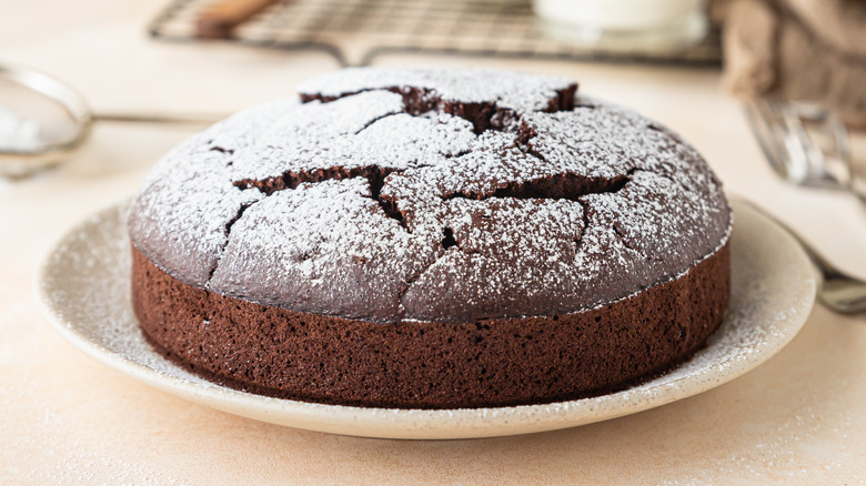 Un pastel de chocolate de una sola capa recubierto con azúcar en polvo sobre un plato blanco
