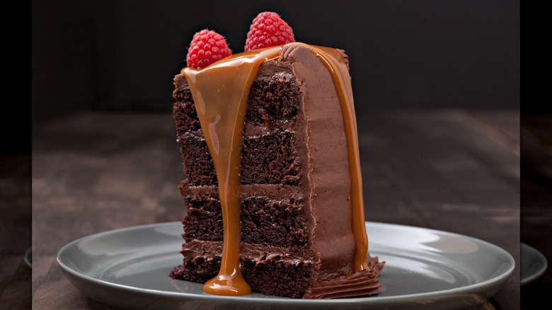 Un trozo de pastel de chocolate cubierto con caramelo y frambuesas, servido en un plato de plata