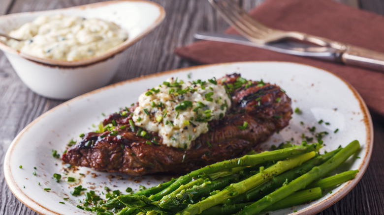 Filete con mantequilla de queso azul en un plato con espárragos