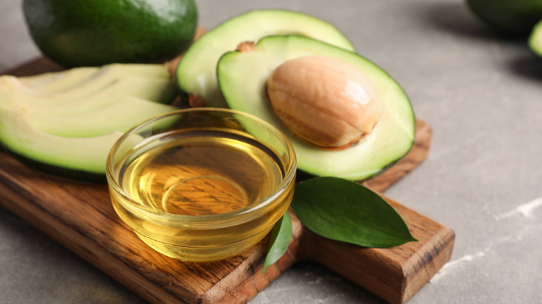 Un recipiente de vidrio con aceite de aguacate con aguacates al fondo